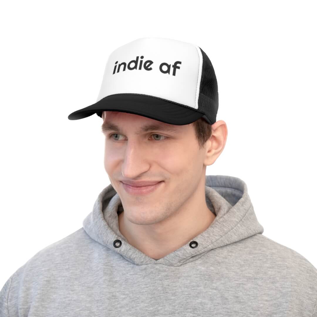 A man in a gray hoodie wears the Indie AF Trucker Hat, featuring a bold black and white design with standout lettering on the front.