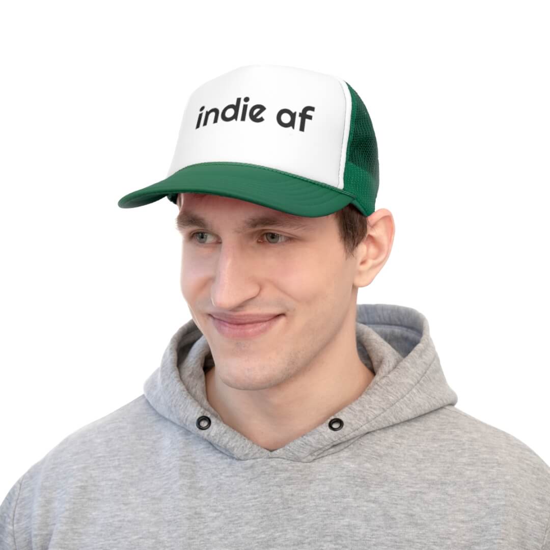 A man wears a gray hoodie and the Indie AF Trucker Hat, featuring a striking green-and-white design with “Indie AF” boldly displayed on the front.