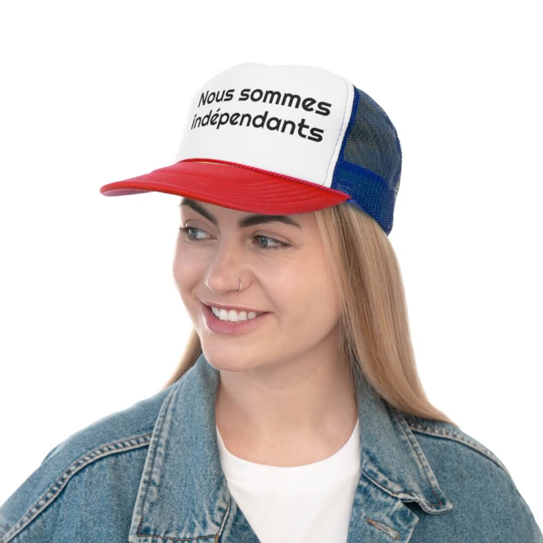 Wearing the Cannes Indie Trucker Hat featuring “Nous sommes indépendants” in red, white, and blue with a denim jacket, this person smiles confidently against a white background—radiating true indie spirit.