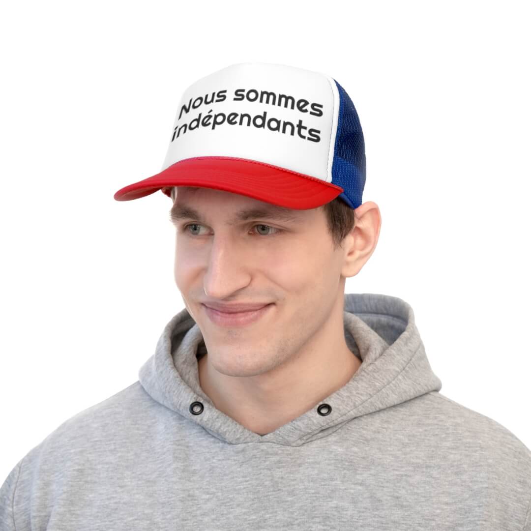 A man in a gray hoodie wears the Cannes Indie Trucker Hat, featuring a tricolor design and Nous sommes indépendants text on the front, set against a white background.