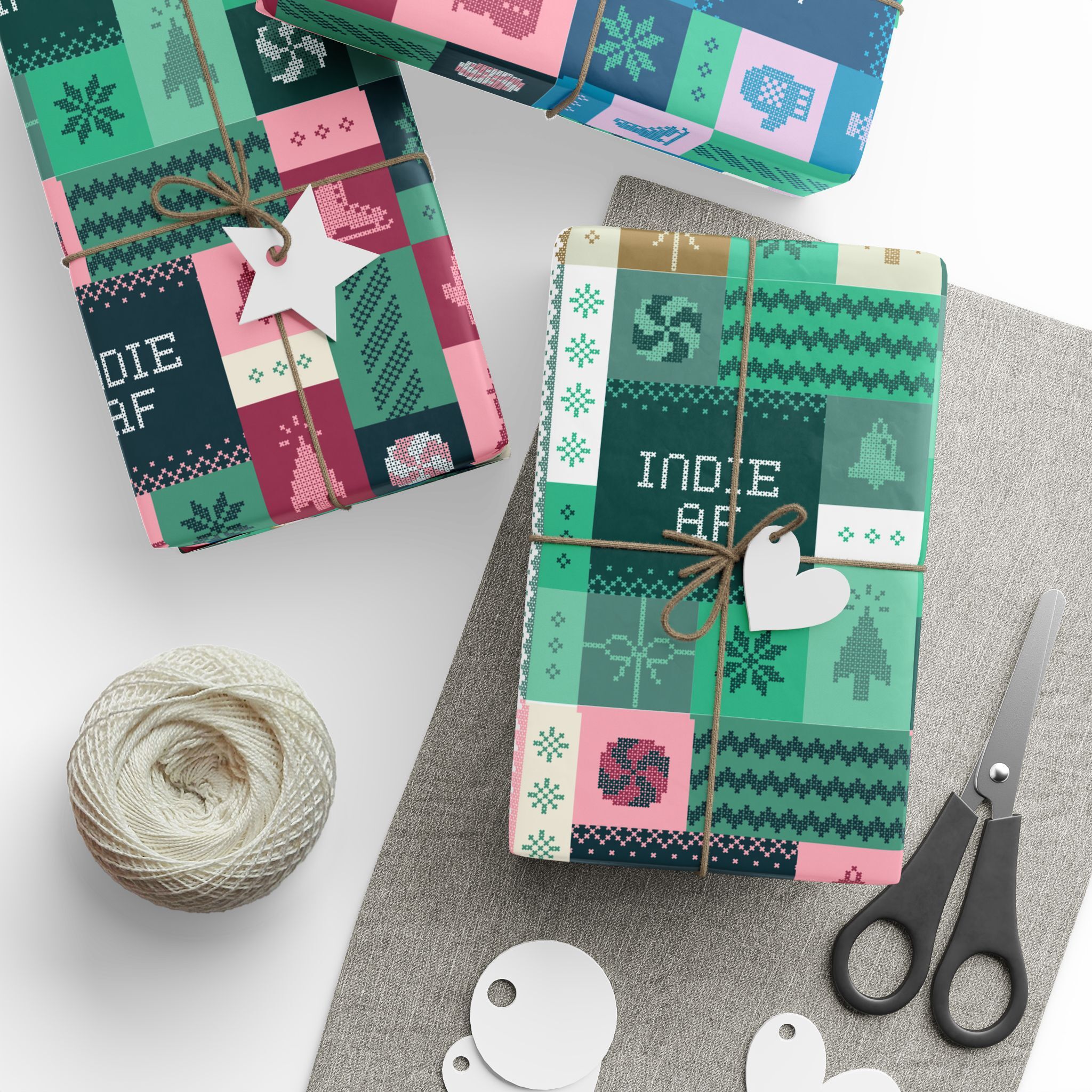 Three gifts wrapped in "Ship It" Wrapping Paper | Indie AF 2025 Holidays by Grown sit on a table with scissors, twine, gift tags, and a gray placemat—all set for holiday gifting with standout indie style.
