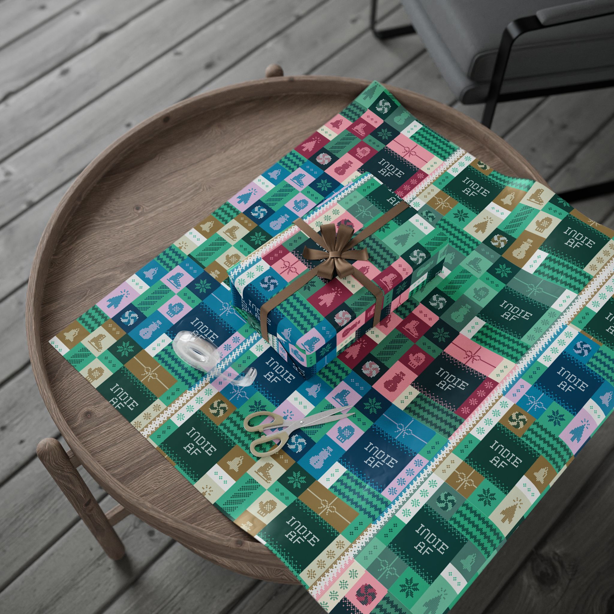 A round wooden table with wrapped gifts, scissors, tape, and "Ship It" Wrapping Paper | Indie AF 2025 Holidays by Grown—festive paper in vibrant holiday patterns, perfect for celebrating the season’s indie spirit.