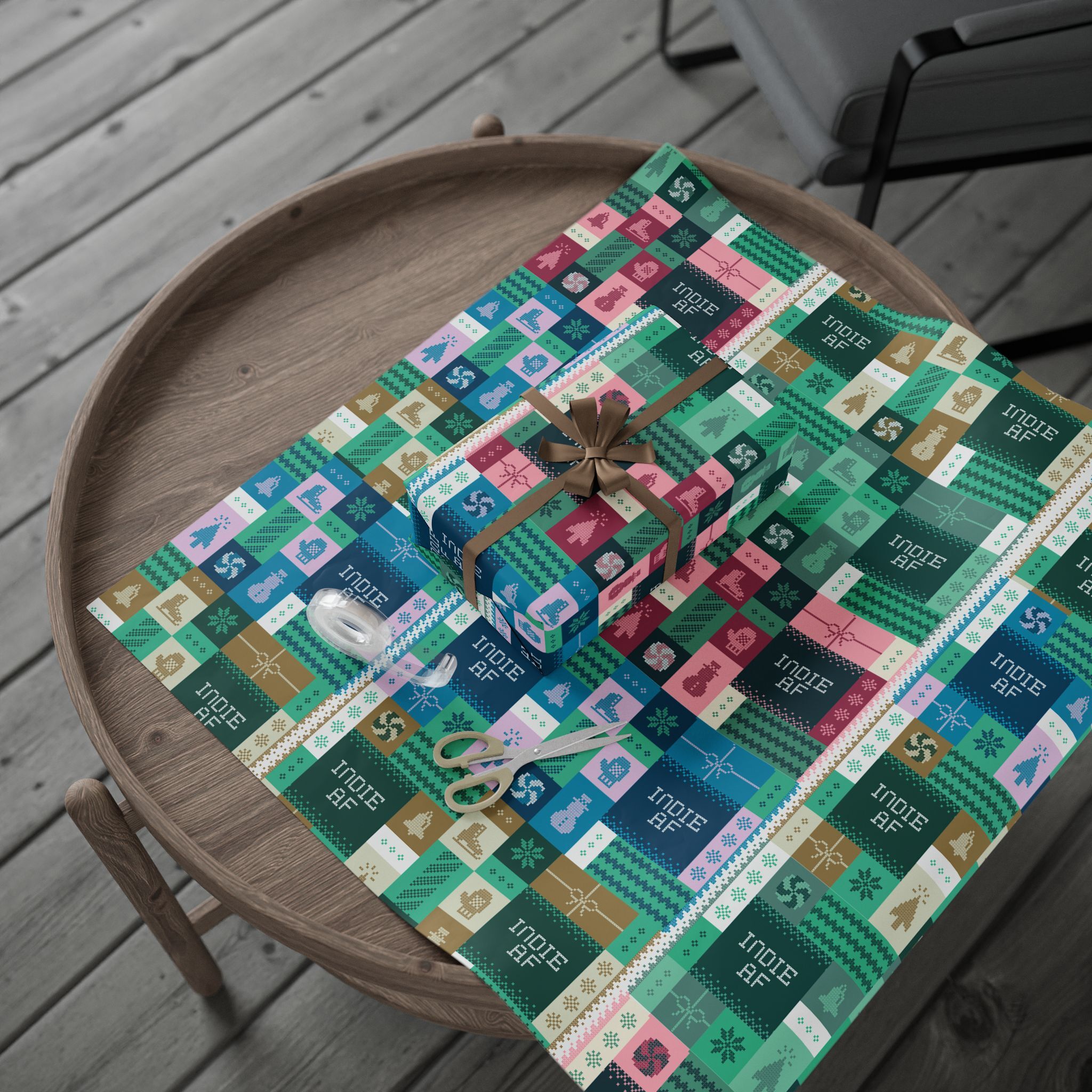 A round wooden table features a wrapped gift, scissors, and tape on vibrant "Ship It" Wrapping Paper | Indie AF 2025 Holidays by Grown—geometric shapes and holiday icons ready to spark festive joy.