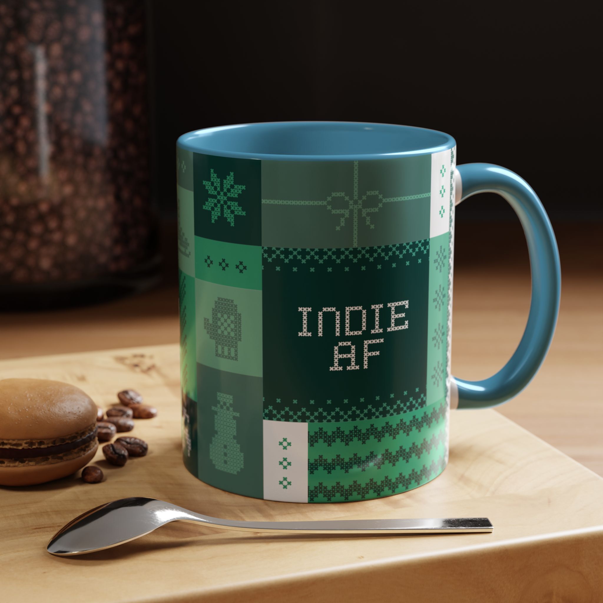 The "Mandatory Fun" Mug - Green (11oz, Indie AF 2025 Holidays by Grown) sits on a wooden surface next to a spoon, a macaron, and scattered coffee beans.