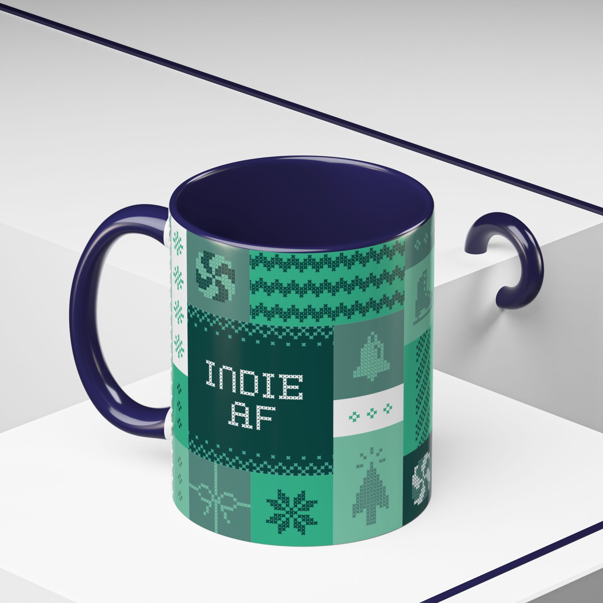 The "Mandatory Fun" Mug - Green | 11oz Indie AF 2025 Holidays by Grown in green and blue with pixel art and INDIE AF 2025 text, displayed on a white geometric surface.