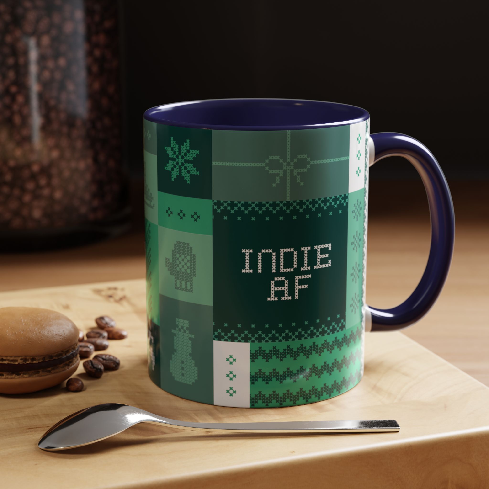 The "Mandatory Fun" Mug - Green | 11oz Indie AF 2025 Holidays by Grown sits on a wooden surface with a macaron, coffee beans, and a metal spoon. Pixel art-style pattern adds charm to this festive mug.