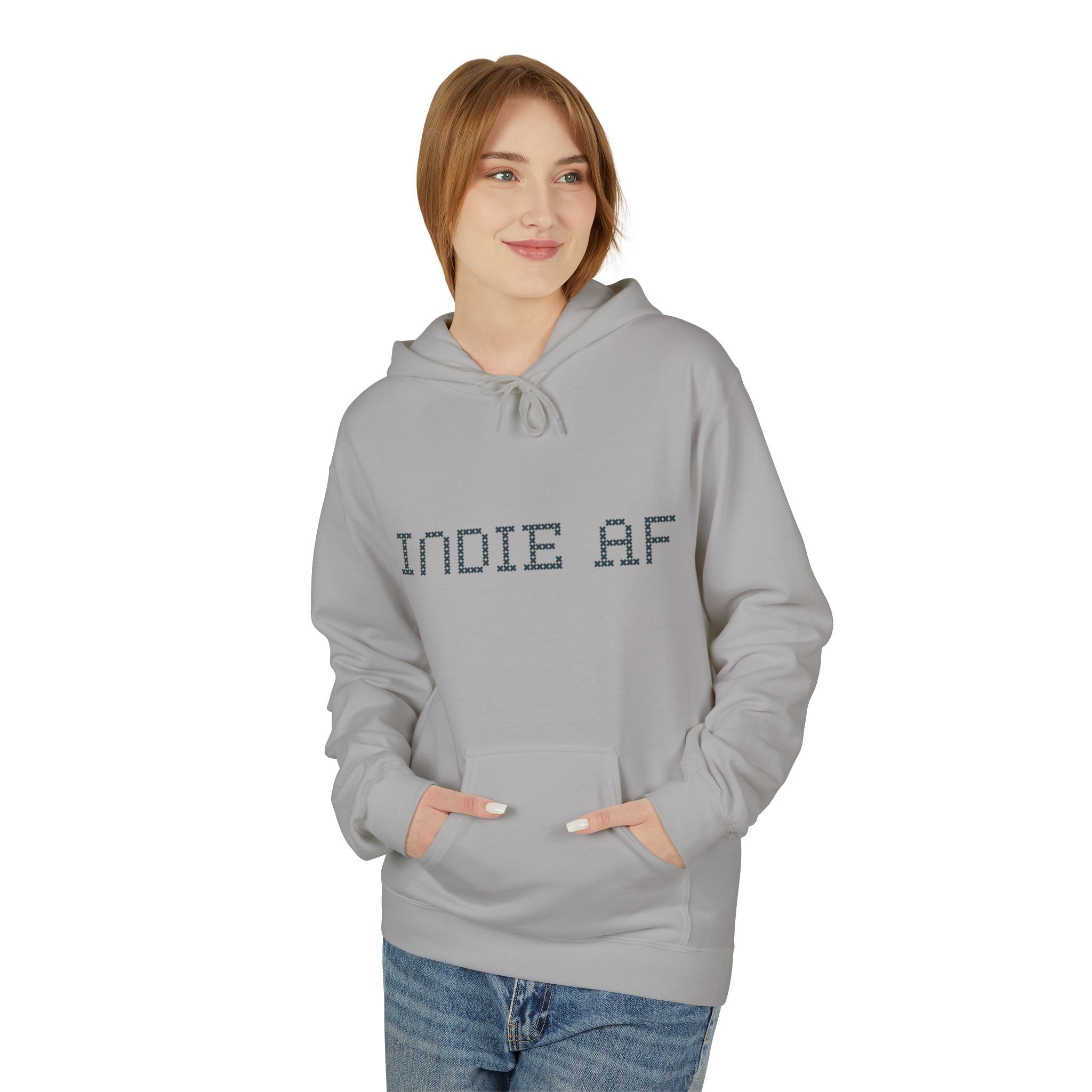 A person wears The "Uniform Rebellion" Hoodie | Indie AF 2025 Holidays by Grown, a light gray hoodie featuring INDIE AF on the front, standing against a white background with hands in pockets and looking to the side.