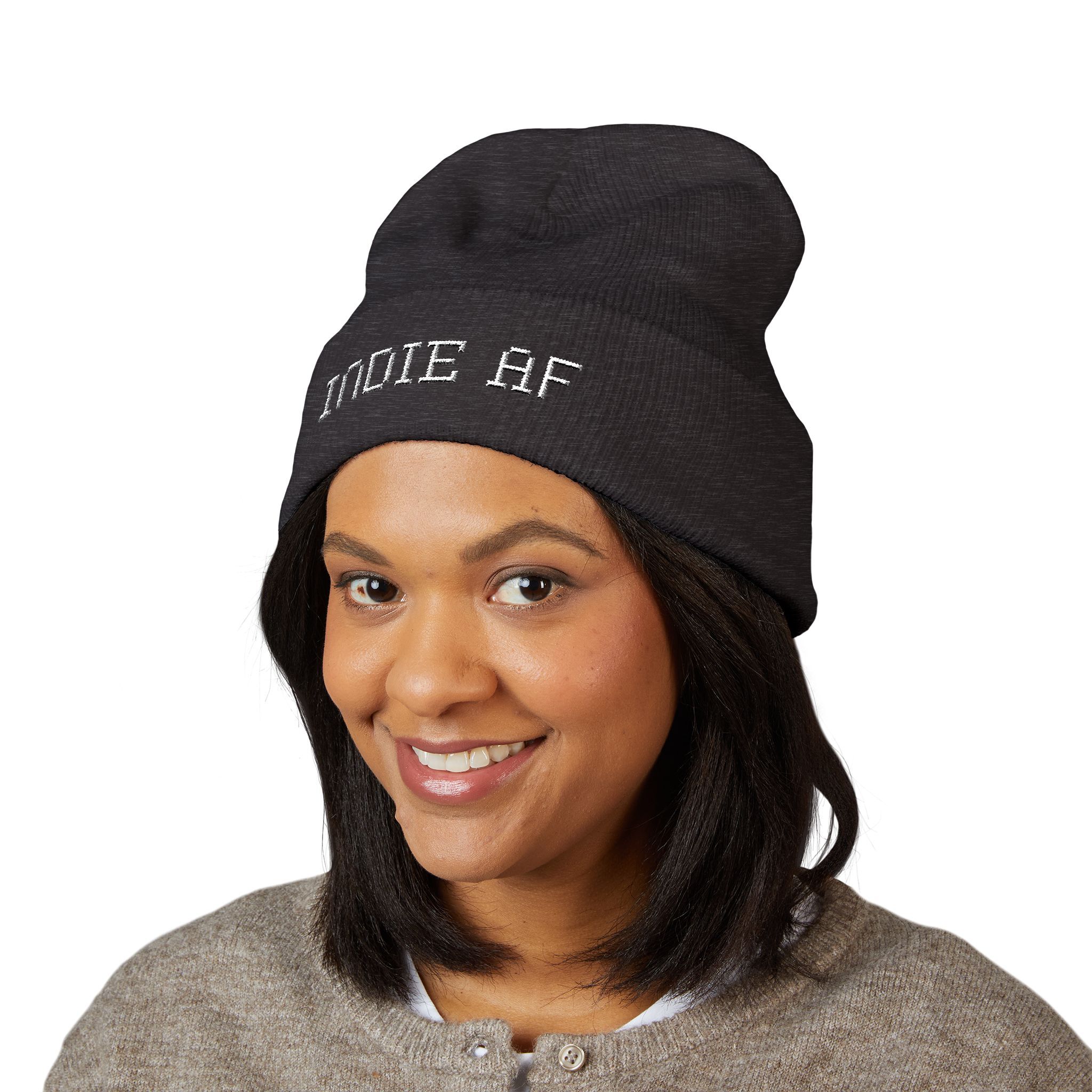 A woman smiles in a gray sweater and The Deep Dive: Indie AF 2025 Holidays by Grown cuffed beanie—black with light "INDIE AF" embroidery—against a white background, perfect for your Indie AF 2025 holiday look.