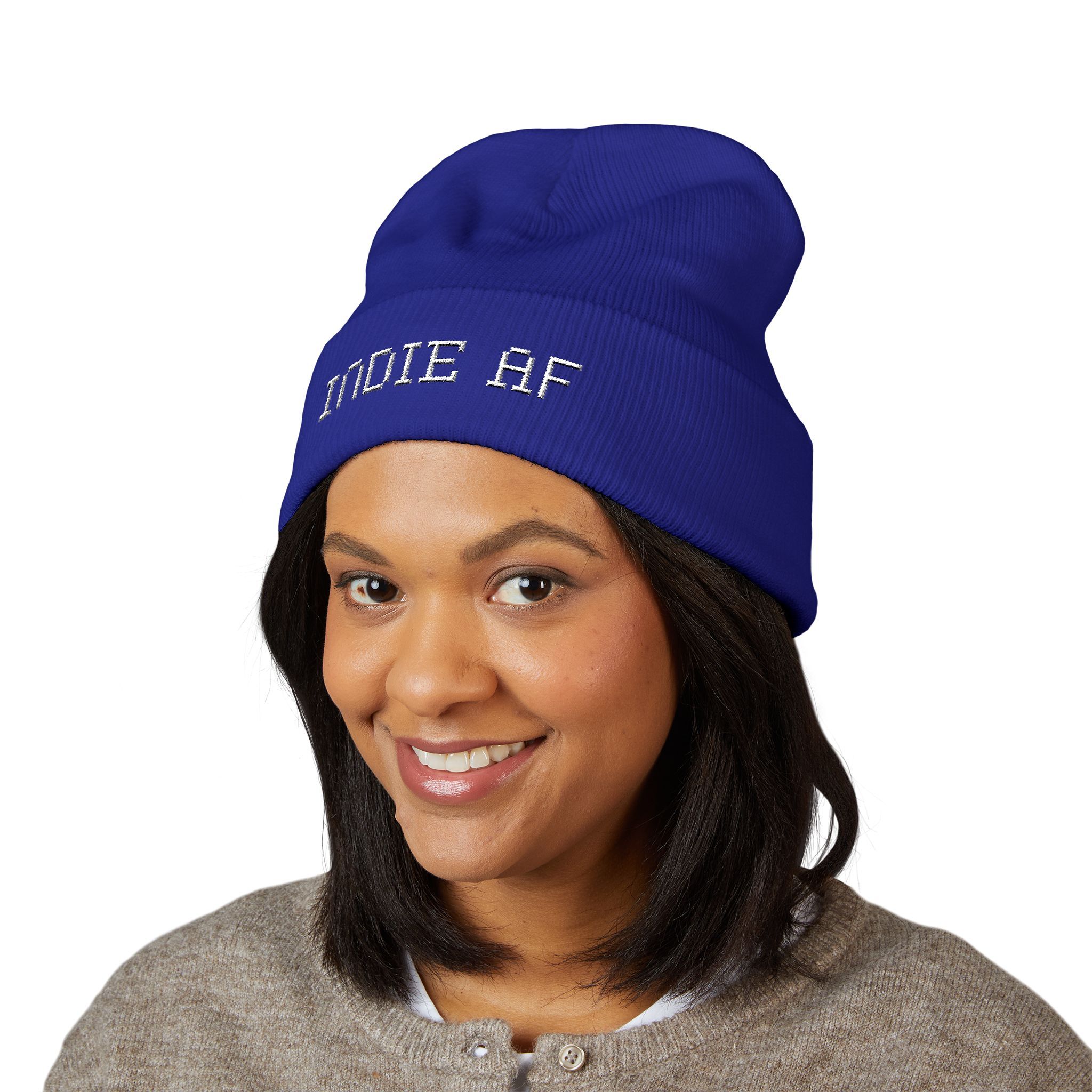 A woman smiles wearing The Deep Dive: Indie AF 2025 Holidays by Grown cuffed beanie, featuring light embroidery, against a plain white background.