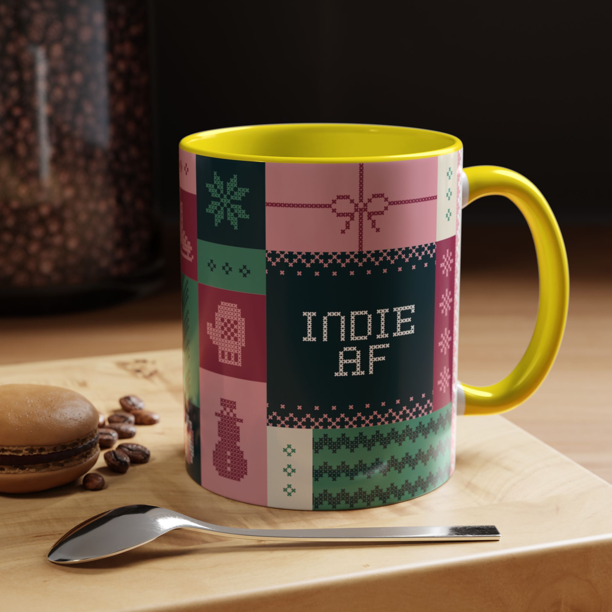 The "Mandatory Fun" Mug - Pink | 11oz Indie AF 2025 Holidays by Grown features vibrant pixel art and "INDIE AF" text, shown on a wooden surface beside a spoon, a macaron, and coffee beans.