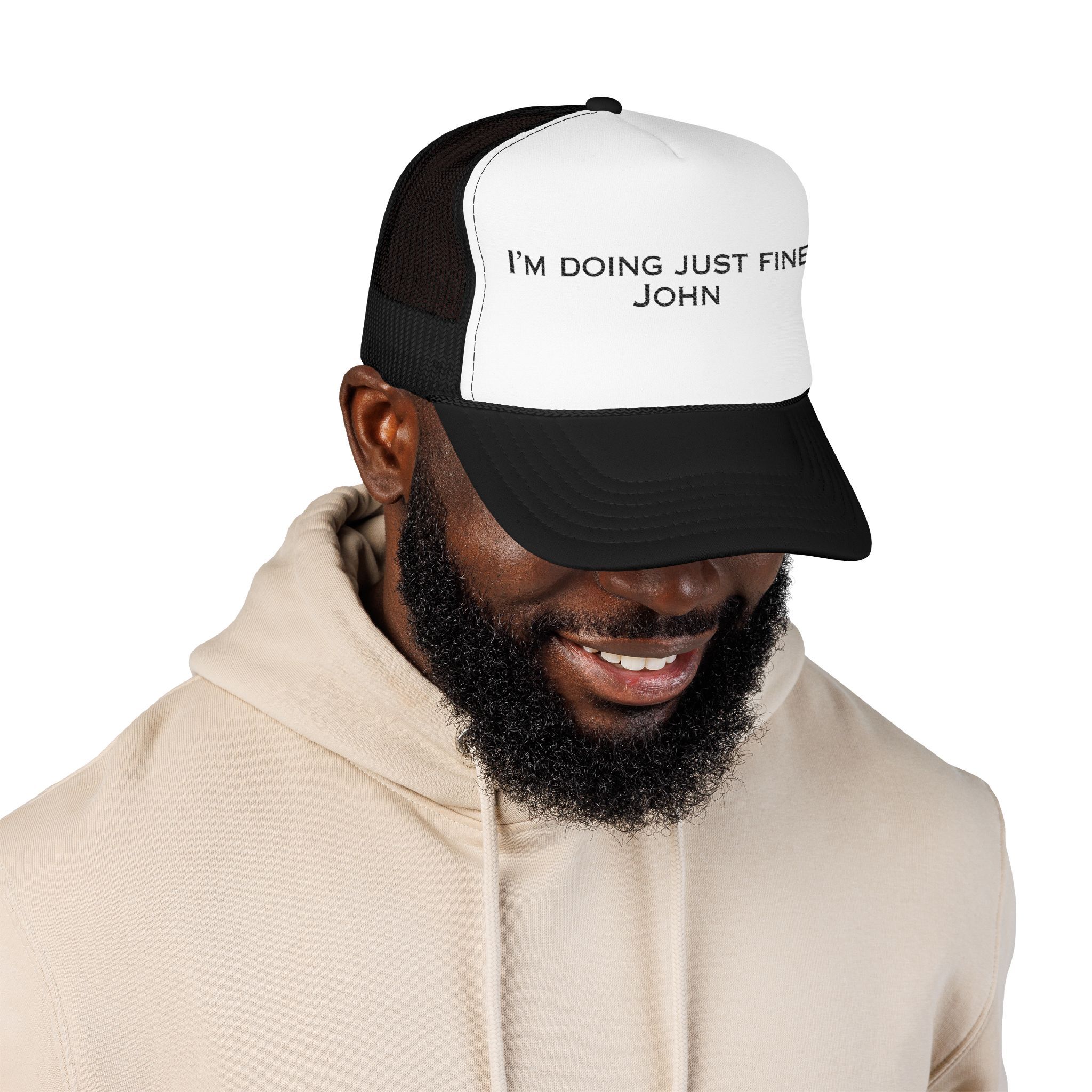 A man wearing a light-colored "I'm Doing Just Fine, John" Trucker Hat smiles as he looks down.