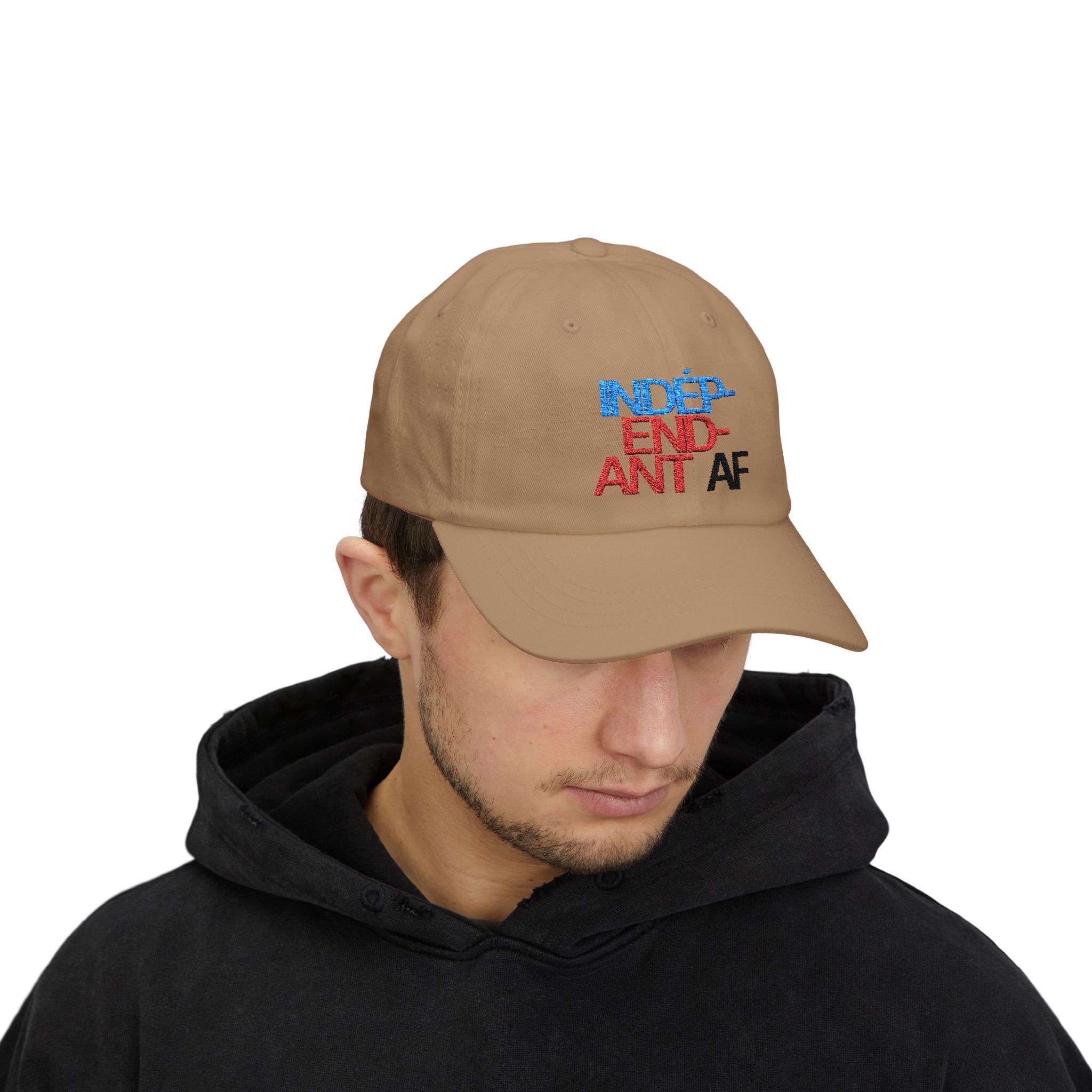 A man in a black hoodie looks down, wearing The Macrons Secret Weakness Baseball Cap—tan with INDEPENDENT AF embroidered in blue, red, and black—subtly hinting at his secret weakness.