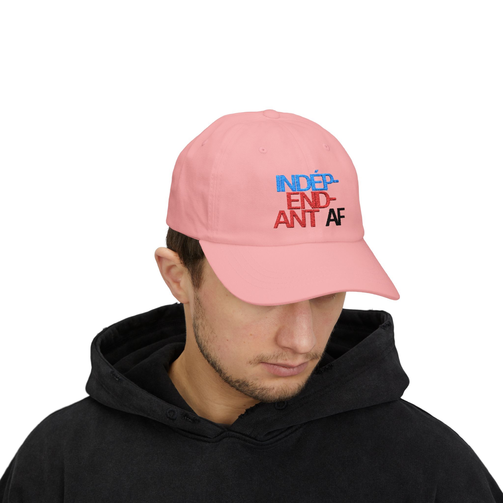 Someone wearing The Macrons Secret Weakness Baseball Cap—pink, with multicolored embroidered text—and a black hoodie, gazes downward as if concealing a hidden vulnerability.