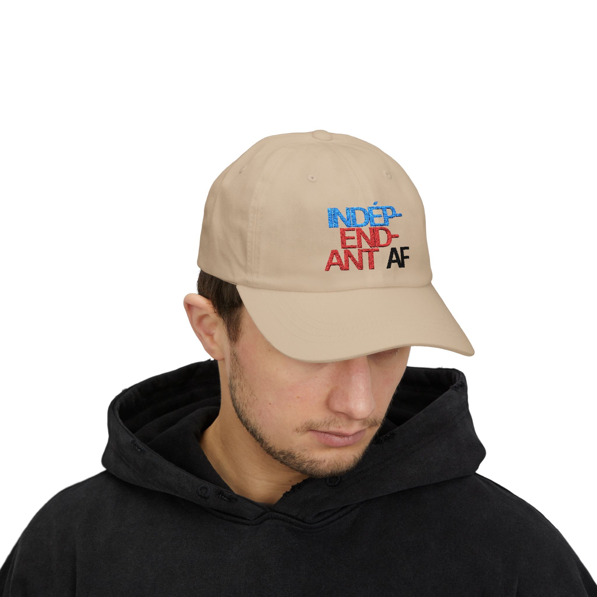 Someone wearing The Macrons Secret Weakness Baseball Cap in beige with blue, red, and black text looks downward in a black hoodie—almost as if theyre hiding a secret weakness.