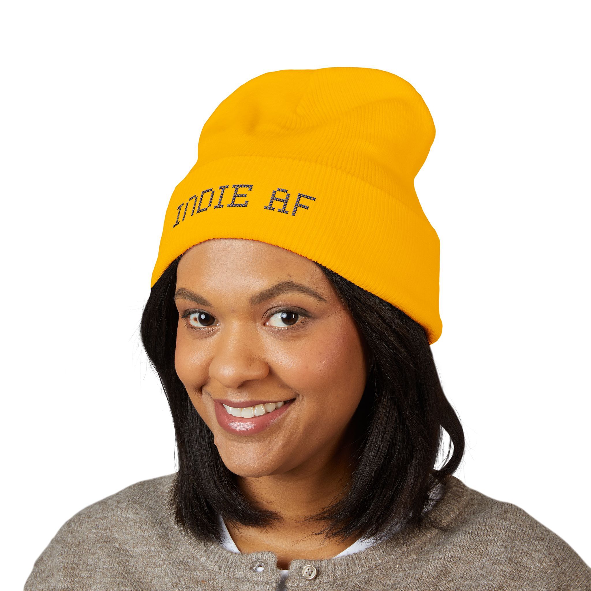 A woman smiles, wearing the Indie AF 2025 Holidays by Grown cuffed beanie with dark embroidery and a grey sweater.
