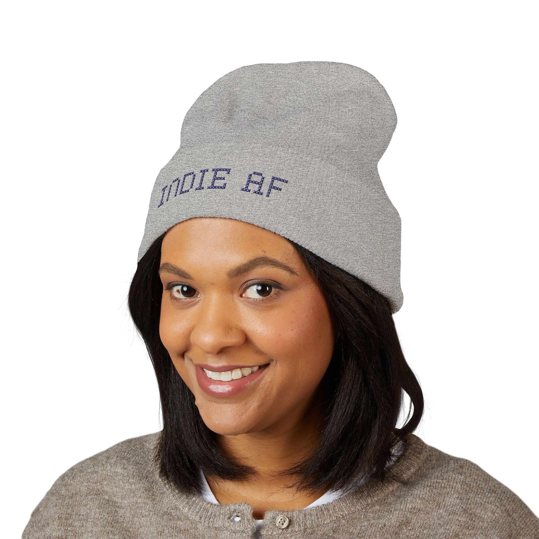 Woman smiling at the camera, wearing the Indie AF 2025 Holidays by Grown cuffed beanie in grey, featuring dark embroidery reading "INDIE AF" on the front.